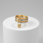 Layered Gold & Silver Safety Pin Ring on a white pedestal against a gray background