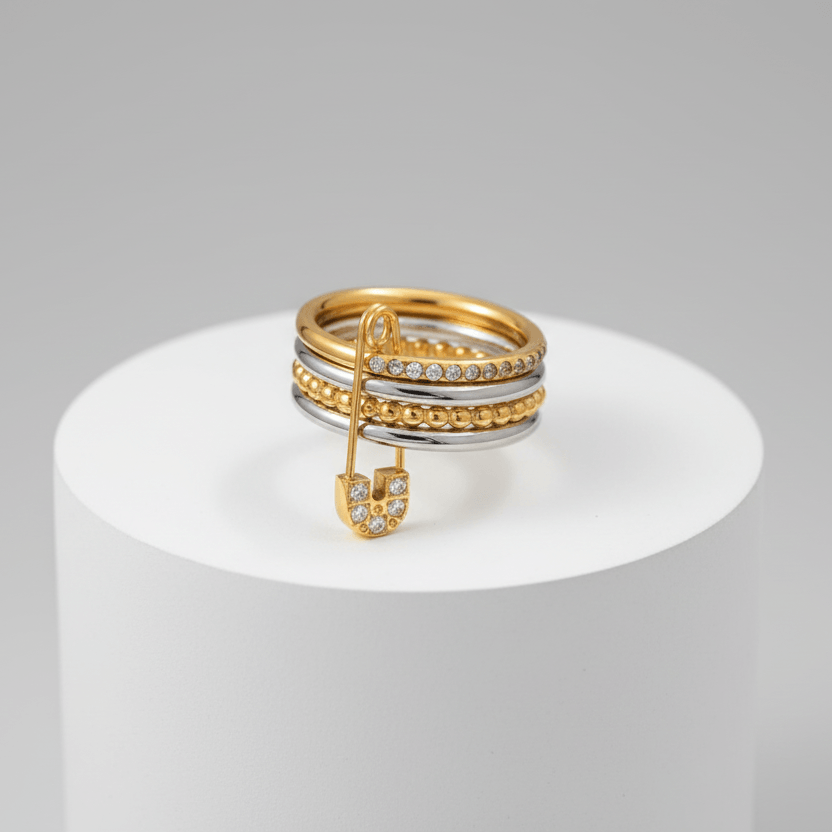 Layered Gold & Silver Safety Pin Ring on a white pedestal against a gray background