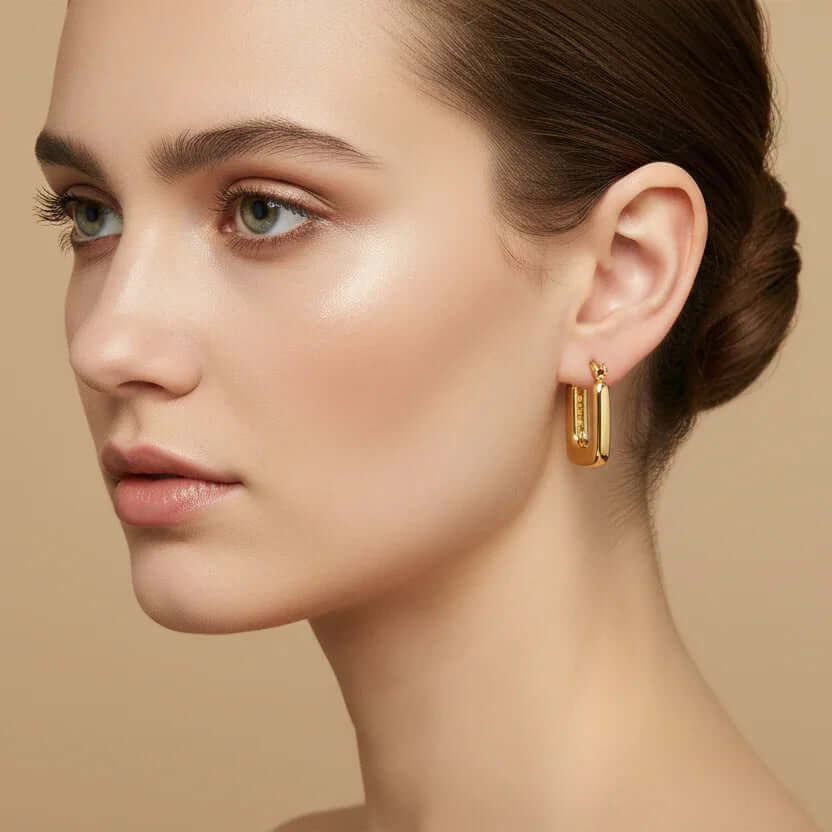 Woman wearing Ceyrah mini gold square hoop earrings with a smooth finish