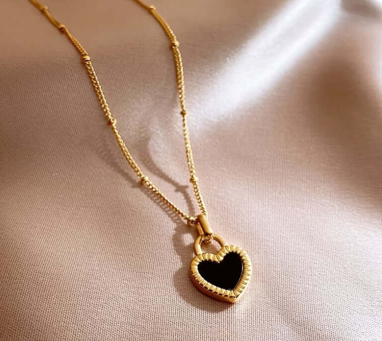 Gold heart pendant necklace with black center on soft satin fabric background