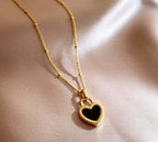 Gold heart pendant necklace with black center on soft satin fabric background