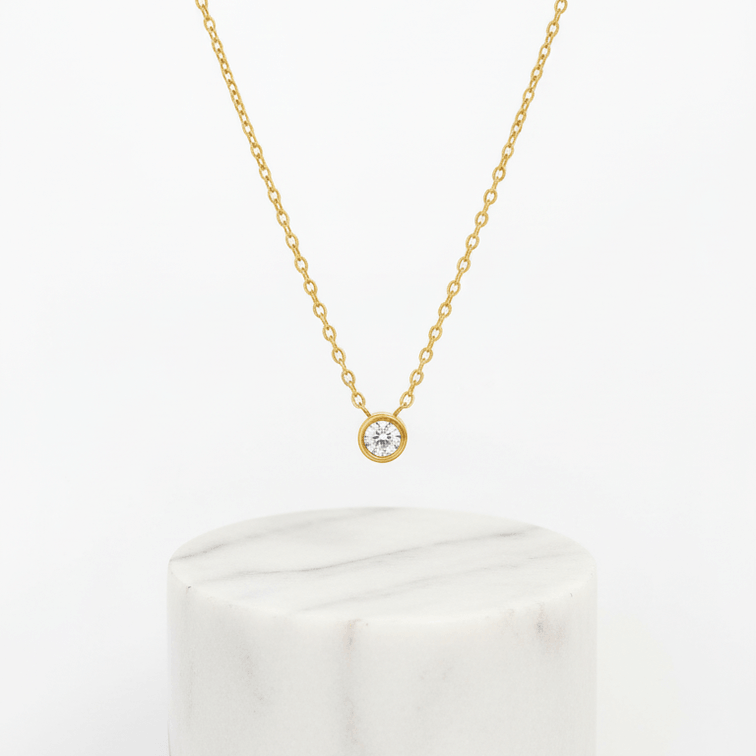 Single Diamond Necklace Gold on white marble pedestal 