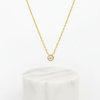 Single Diamond Necklace Gold on white marble pedestal 