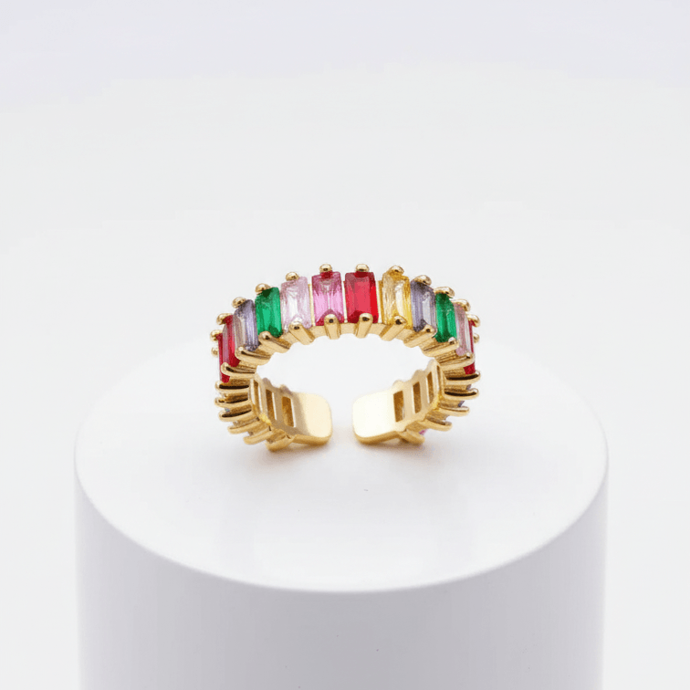 Spectrum Baguette Eternity Ring with colorful gemstones on a white pedestal against a white background