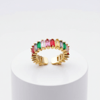 Spectrum Baguette Eternity Ring with colorful gemstones on a white pedestal against a white background