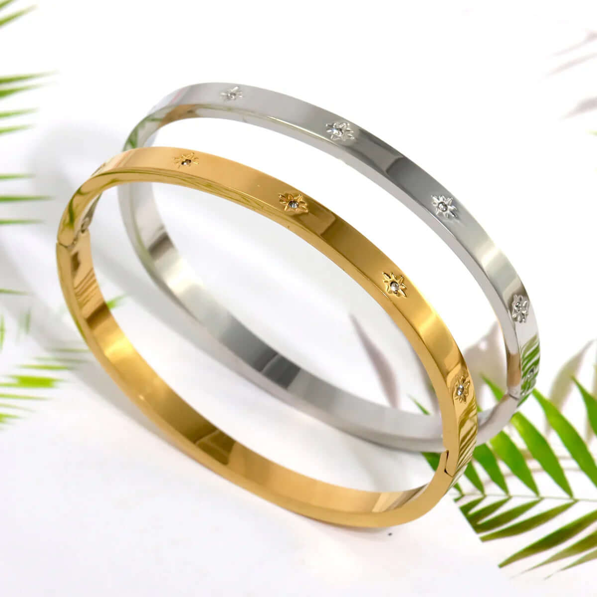 Ceyrah gold and silver Star Zirconia Bangle Bracelet on white background with green leaves