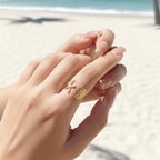 Hand wearing a Starfish & Shell Open Ring Gold on a beach