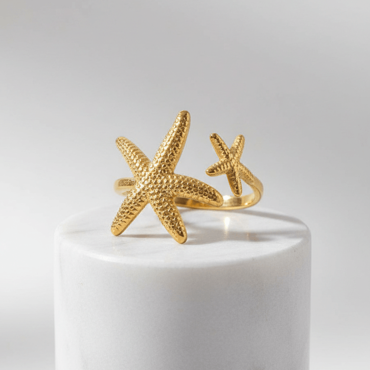 Twin Starfish Open Gold Ring on a white cylindrical stand with a light gray background