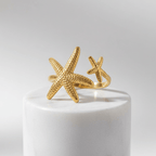 Twin Starfish Open Gold Ring on a white cylindrical stand with a light gray background