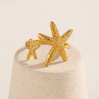 Twin Starfish Open Gold Ring on a beige stone surface