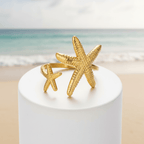 Twin Starfish Open Gold Ring on a white pedestal against a white background