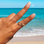 Hand wearing a Twin Starfish Open Gold Ring with a beach background
