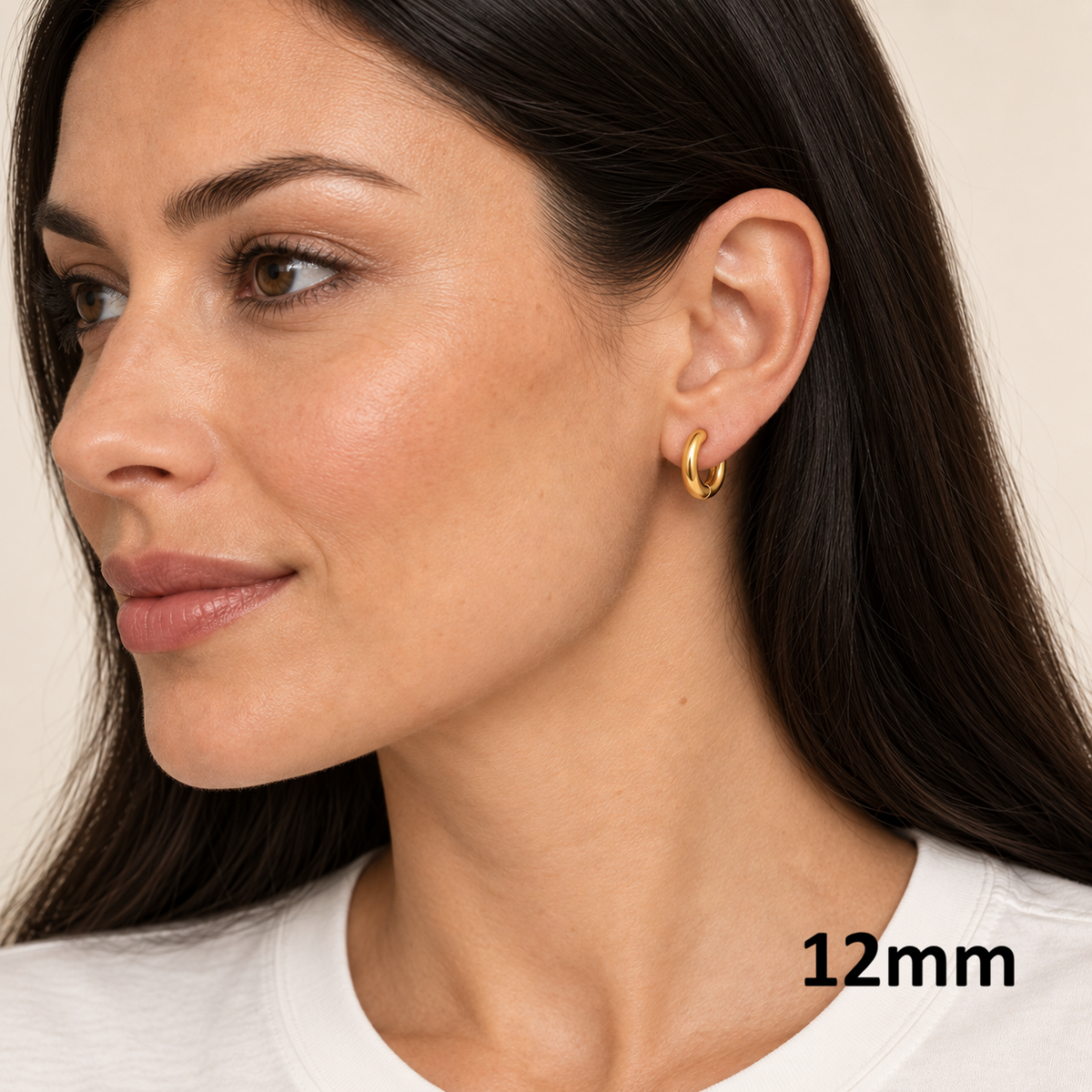 A close-up of a woman wearing a small gold hoop earring, with the text '12mm' in the bottom right corner. The background is a soft, warm off-white.