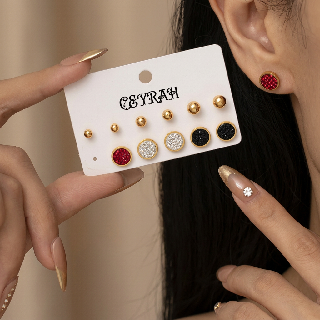 A close-up of a person wearing a pair of Waterproof Gold Circle Stud Earrings Set with red and black textured centers, while another hand holds a white display card showing additional matching earrings. The card is branded 'CEYRAH'.