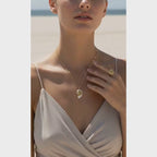 Model wearing a Gold Conch Shell Pendant Necklace and ring on the beach, showcasing coastal elegance.