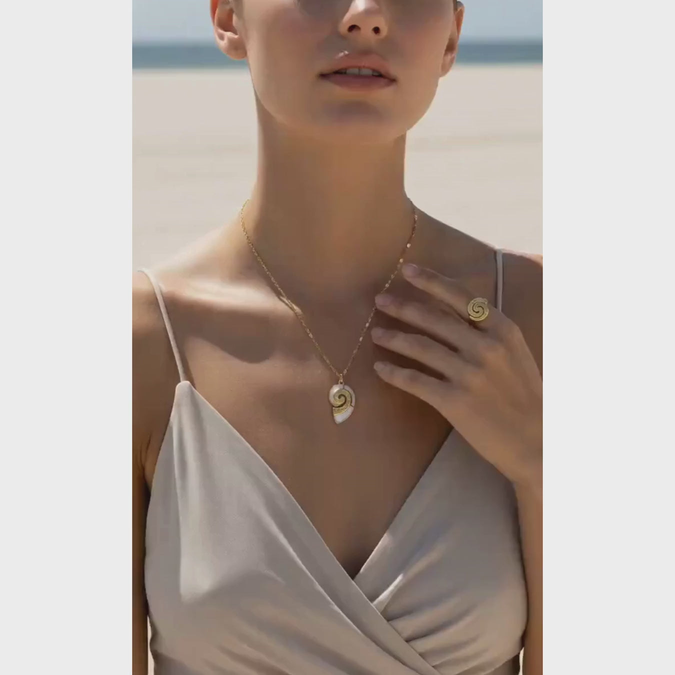 Model wearing a Gold Conch Shell Pendant Necklace and ring on the beach, showcasing coastal elegance.